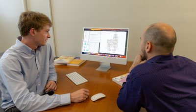 Two students working on a computer, looking at data visualizations and code on the screen.