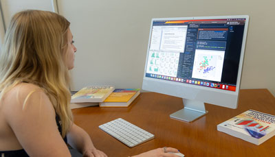 A student working on a computer, looking at data visualizations and code on the screen.