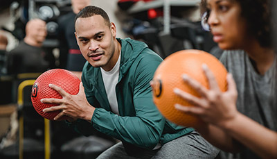Two people in a gym working out with medicine balls.