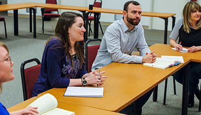 Students sitting in tables listening to a lecture.