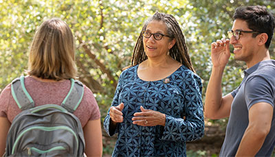  A professor talking with a group of students outside on a sunny day.