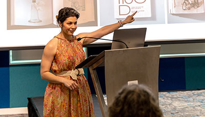 Art history professor giving a lecture at the front of a class in front of a presentation.