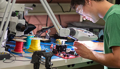 Student examining a device under a magnifying lens.