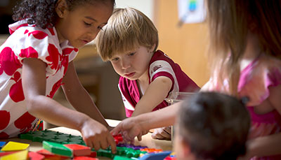 Several young children playing together with a toy on a table. 