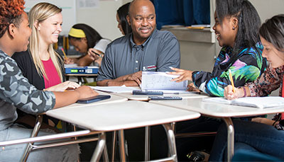 A teacher and education student working with a group of middle school students at a table. 