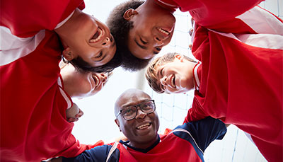Looking up at the smiling faces of a group of young kids and the coach from the middle of a huddle. 