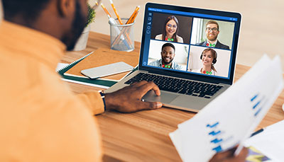 Person sitting at a laptop with a video conference on the screen.