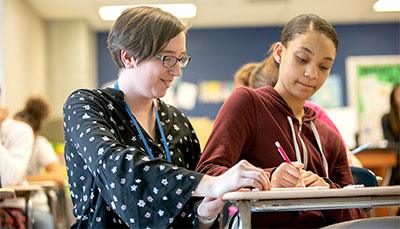Teacher working with a student at their desk.