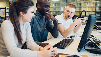 Three students sitting together at a table working on a computer. 