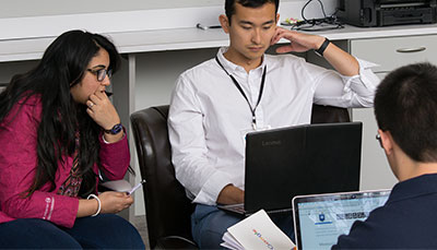 Three students working together in a office with laptops.