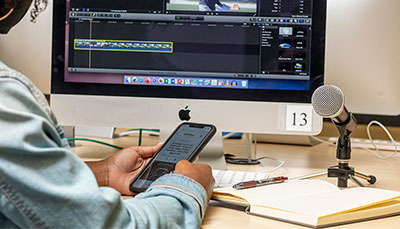 Person holding a phone in front of a computer and a microphone. 